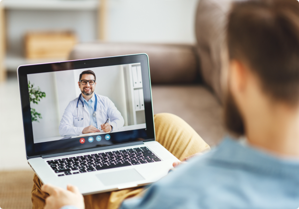 Un jeune homme assis chez lui qui prend part à une consultation en ligne par vidéo-conférence avec un médecin